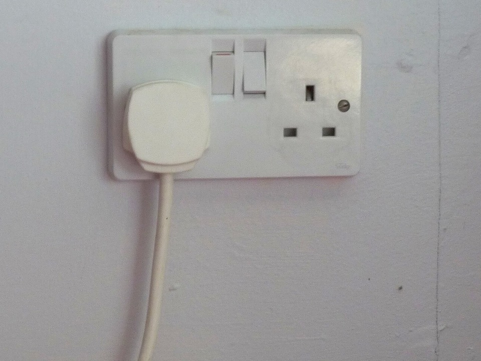 A white switched double socket on a painted indoor wall with one plug in use