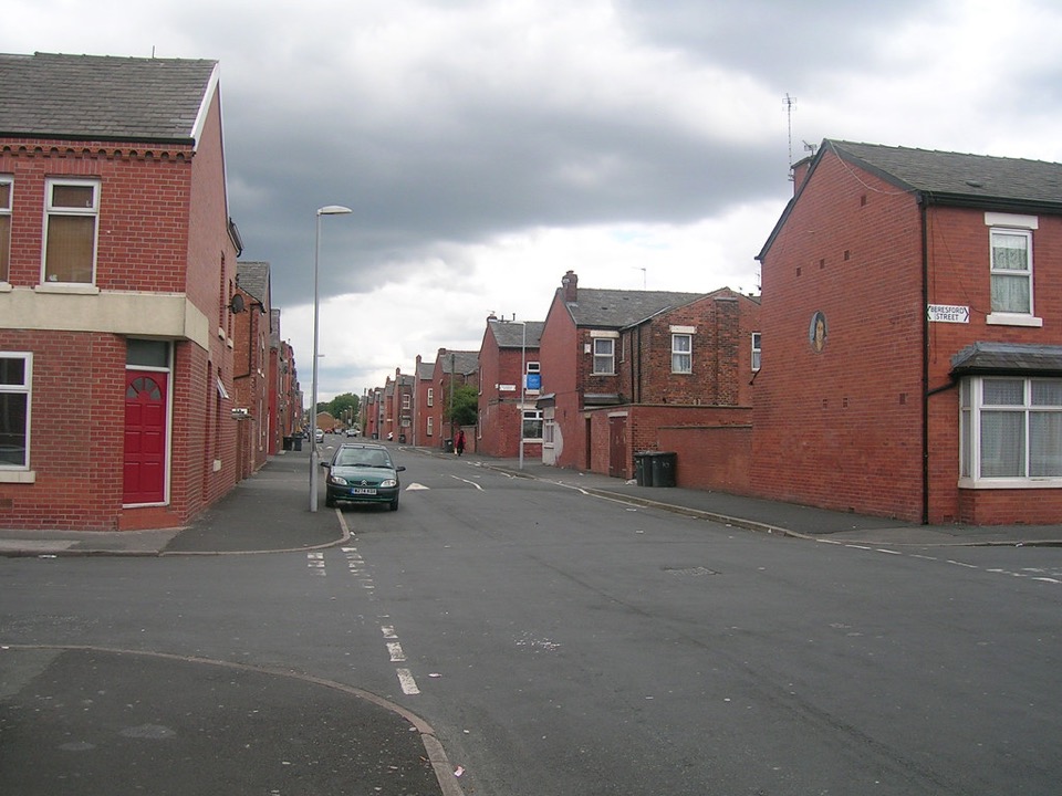 Red brick terraced houses at a street corner under grey cloud